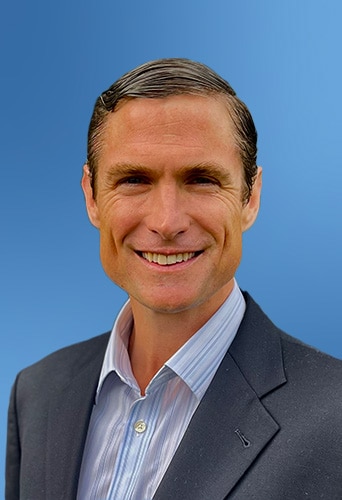 A smiling man wearing a dark blazer and a blue striped shirt, representing software for insurance carriers, against a blue background.